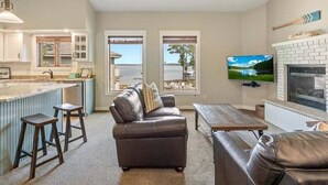 Una sala de estar con sofá, una mesa de centro y televisor. Hay una zona de cocina con barra y taburetes.