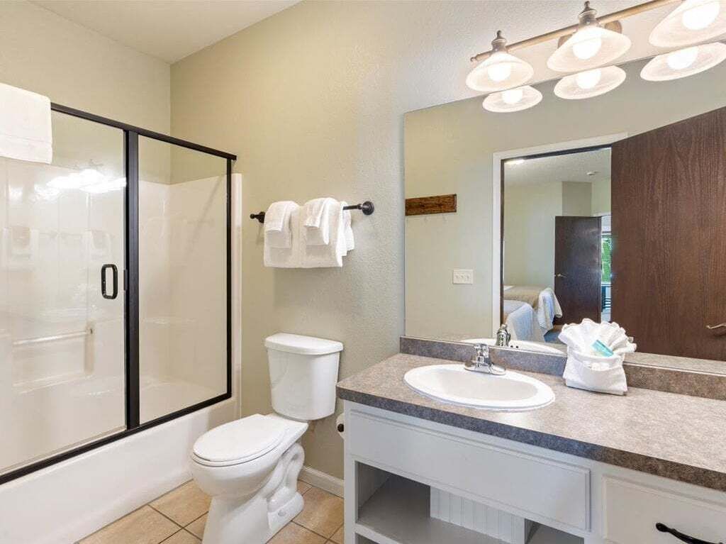 Een badkamer met een douchecabine van glas, een wit toilet, een wastafel met spiegel en een handdoekrek.