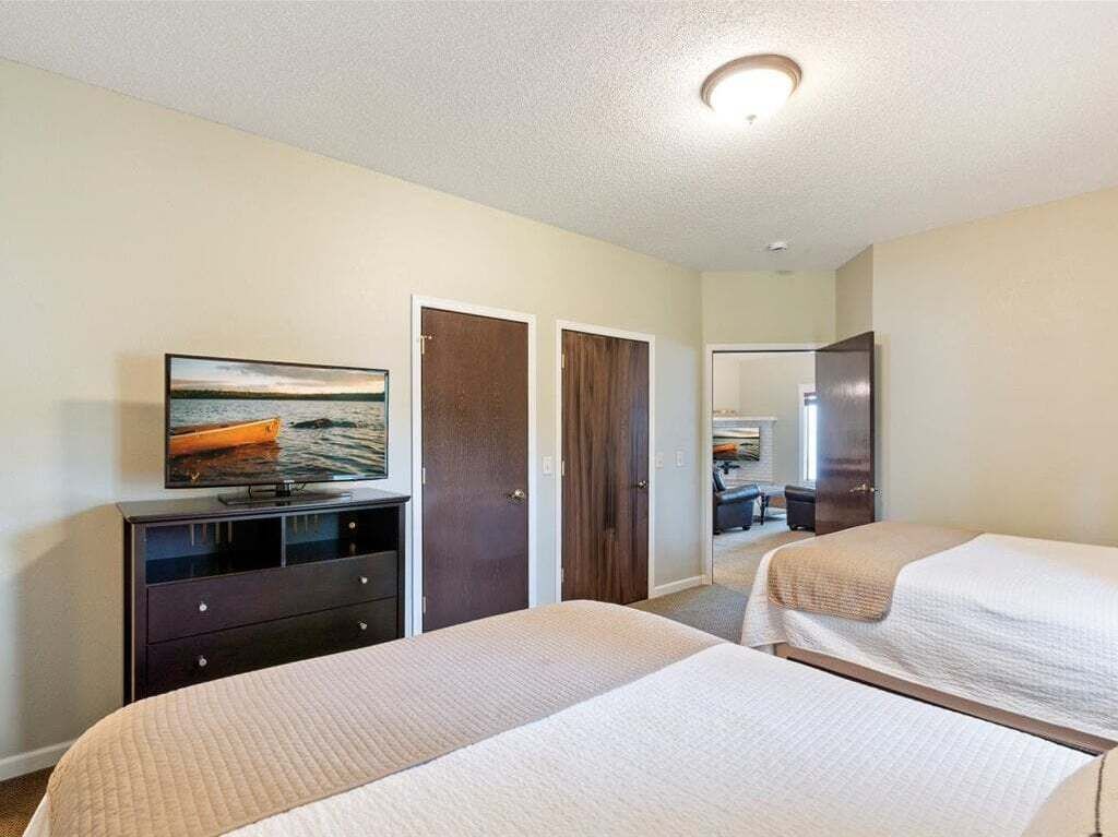 Una habitación de hotel con dos camas, un televisor sobre un tocador y una puerta que da a otra habitación.
