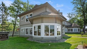 A two-story house with a large bay window, a stone retaining wall, and a well-maintained lawn. - Front Row Seat to Gull Lake Beach | Waterfront Condo (Nisswa)
