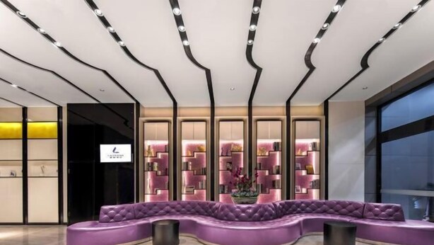 Una hall moderna con un'area salotto curvo color viola, una parete decorata con mensole rosa e un'ampia finestra alla destra.