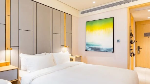 Habitación de hotel con una cama grande, una mesita de noche, un cuadro colgado en la pared y una puerta con manija.