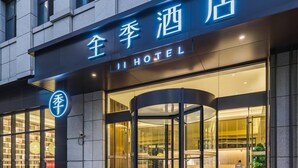 Entrada de hotel con puerta giratoria, un letrero con caracteres chinos y fachada de vidrio.