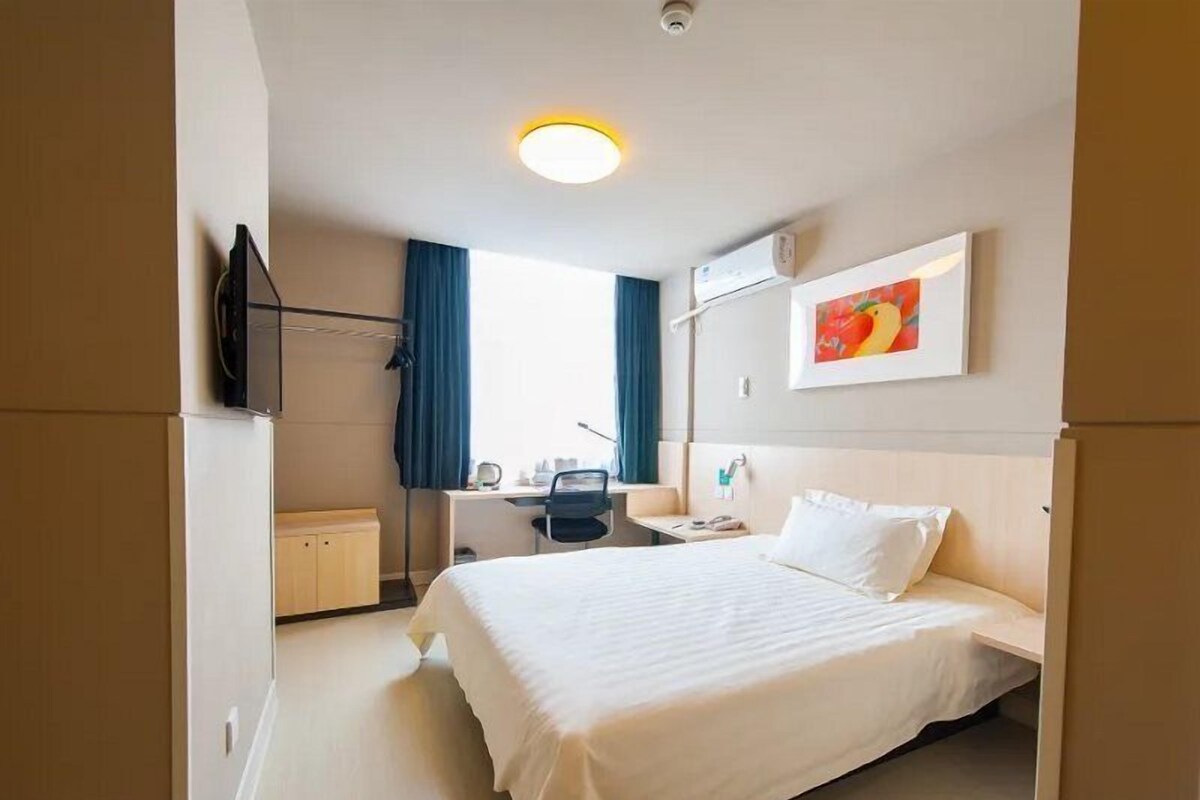 Hotelkamer met een bed, bureau, stoel, raam met gordijnen, airconditioning en een schilderij aan de muur.