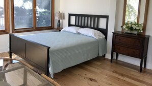 Un dormitorio con cama, cómoda, espejo y ventana con vistas a árboles.
