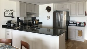 Una cocina moderna con armarios blancos, una isla central, electrodomésticos de acero inoxidable y una encimera negra.