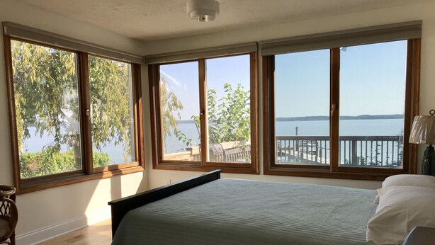 Un dormitorio con cama, suelo de madera y ventanas amplias que ofrecen vista a un lago y un muelle.