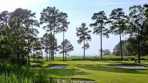Un campo de golf con búnkeres de arena, cielo despejado y un cuerpo de agua al fondo.
