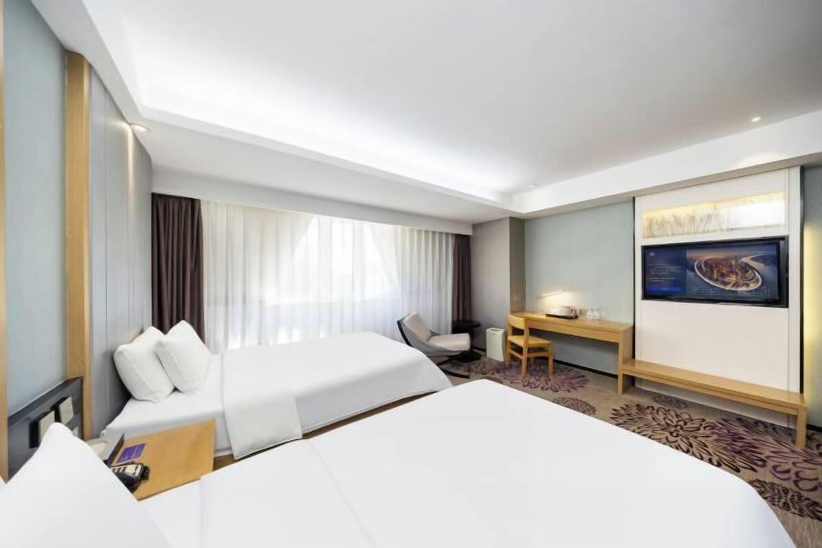 A hotel room with two beds, a desk, a chair, and a television.
