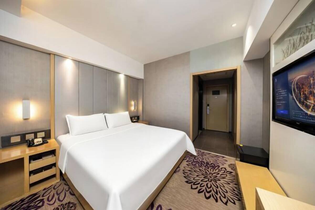 A modern hotel room with a large bed, bedside tables, a flat-screen TV, and a carpet with a floral pattern.