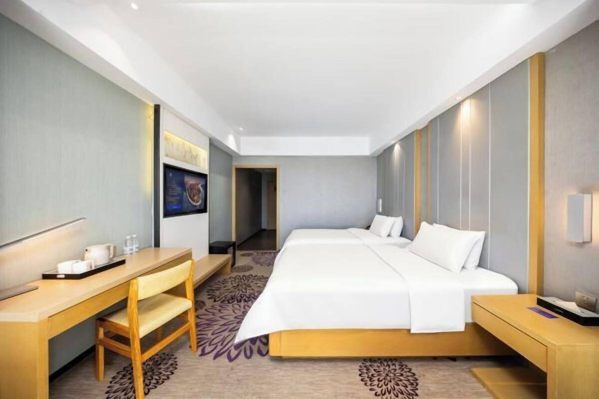 A hotel room with a bed, a desk, a chair, a small table, and a wall-mounted TV.