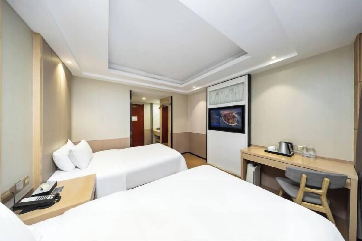 A hotel room with two beds, a desk, a chair, a TV, and a door leading to another room.