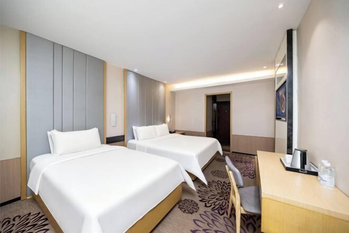 A hotel room with two beds, a desk with a chair, a mirror, and a door leading to another room.
