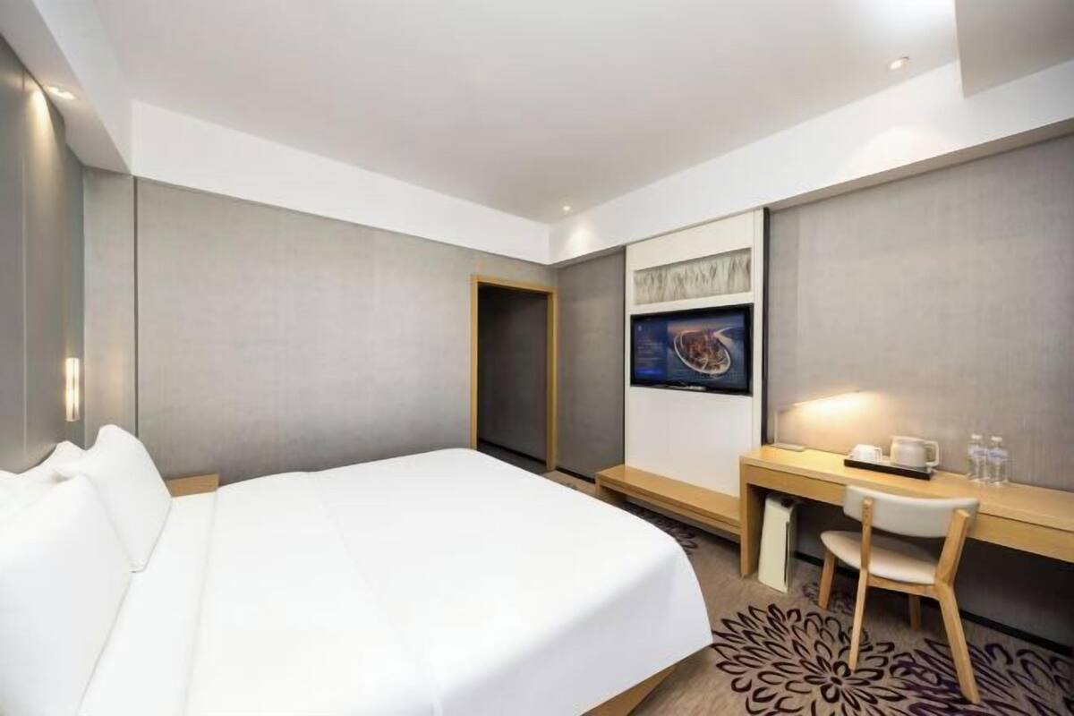 A hotel room with a bed, a desk, a chair, a small table, a picture on the wall, and a carpet with a floral pattern.
