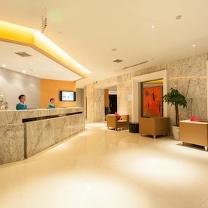 A hotel reception area with a marble reception desk, seating area, and a large painting on the wall.