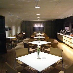 A restaurant with multiple tables and chairs, a counter with a display, and a television screen on the wall.