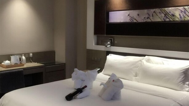 A hotel room with a neatly made bed, a bedside table with a kettle and a tray, and a wall-mounted TV. - Lavande Hotel (Tianjin)
