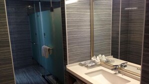 A modern bathroom with a glass shower enclosure, a large mirror, and a sink with toiletries. - Lavande Hotel (Tianjin)