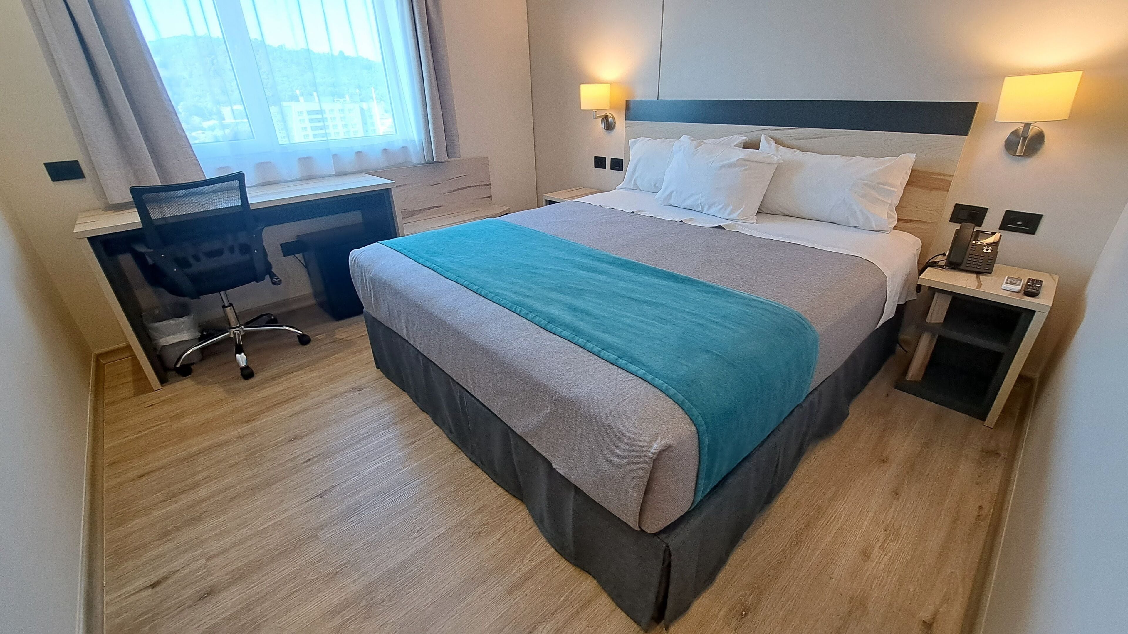 A hotel room with a bed, desk, chair, and bedside lamps.