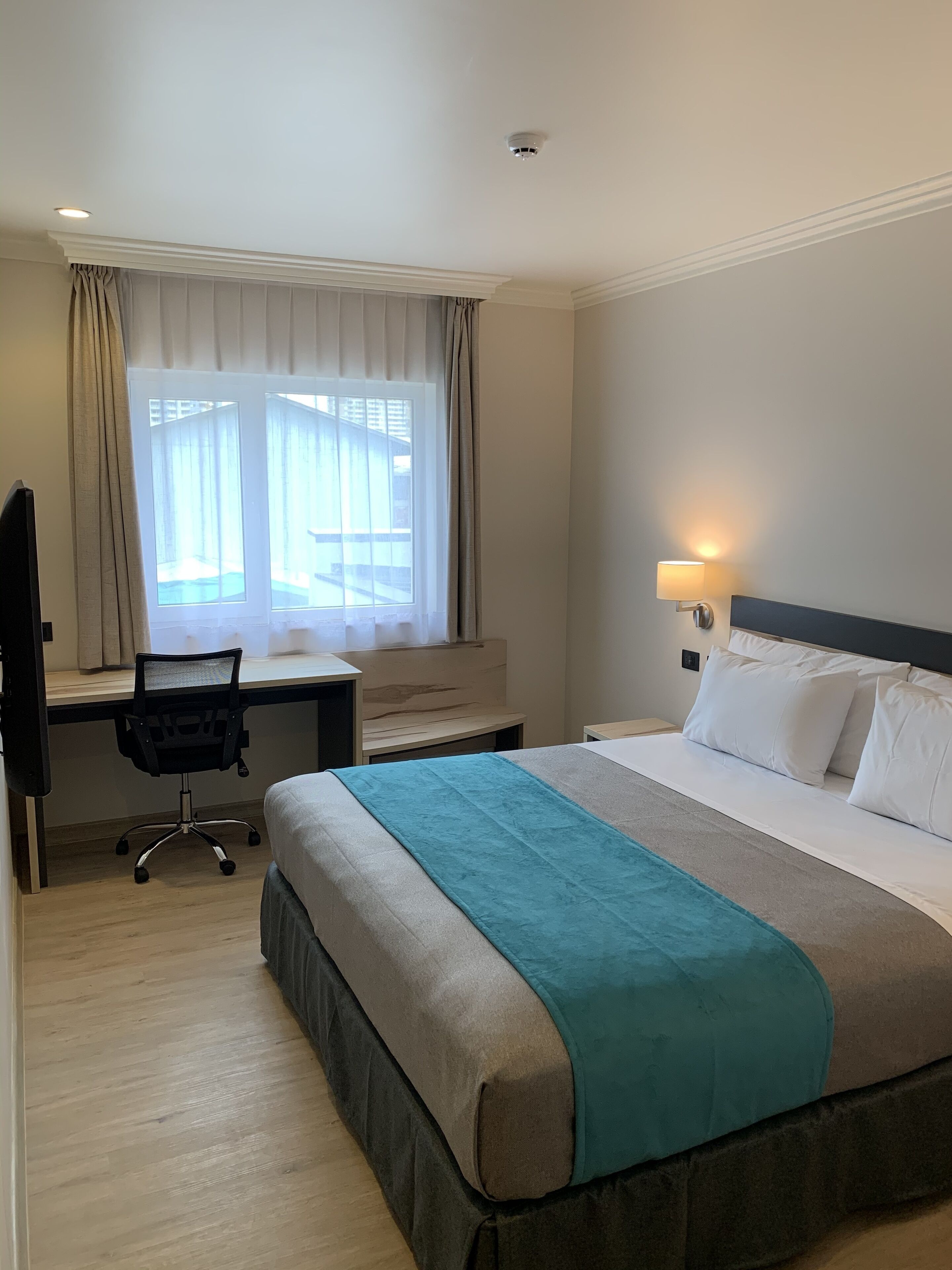 A hotel room with a bed, desk, chair, and a window with curtains.