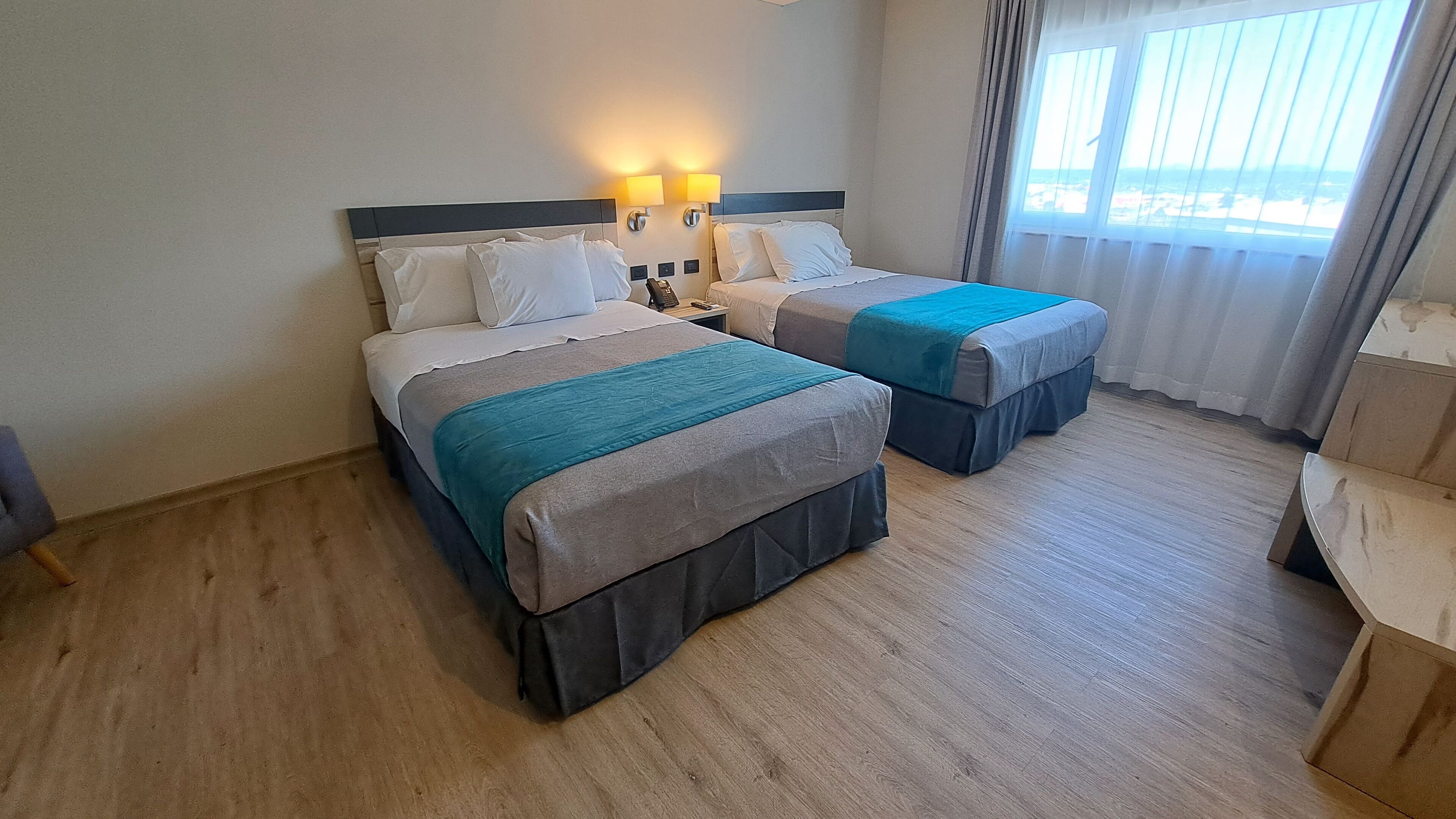 Habitación de hotel con dos camas, una mesita de noche con teléfono y vista a la playa desde la ventana.