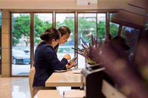 Dos personas sentadas a una mesa con vista a la ventana, una computadora portátil y un teléfono inteligente.