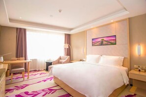 Habitación de hotel con cama, escritorio, silla, mesita de noche y un cuadro en la pared.