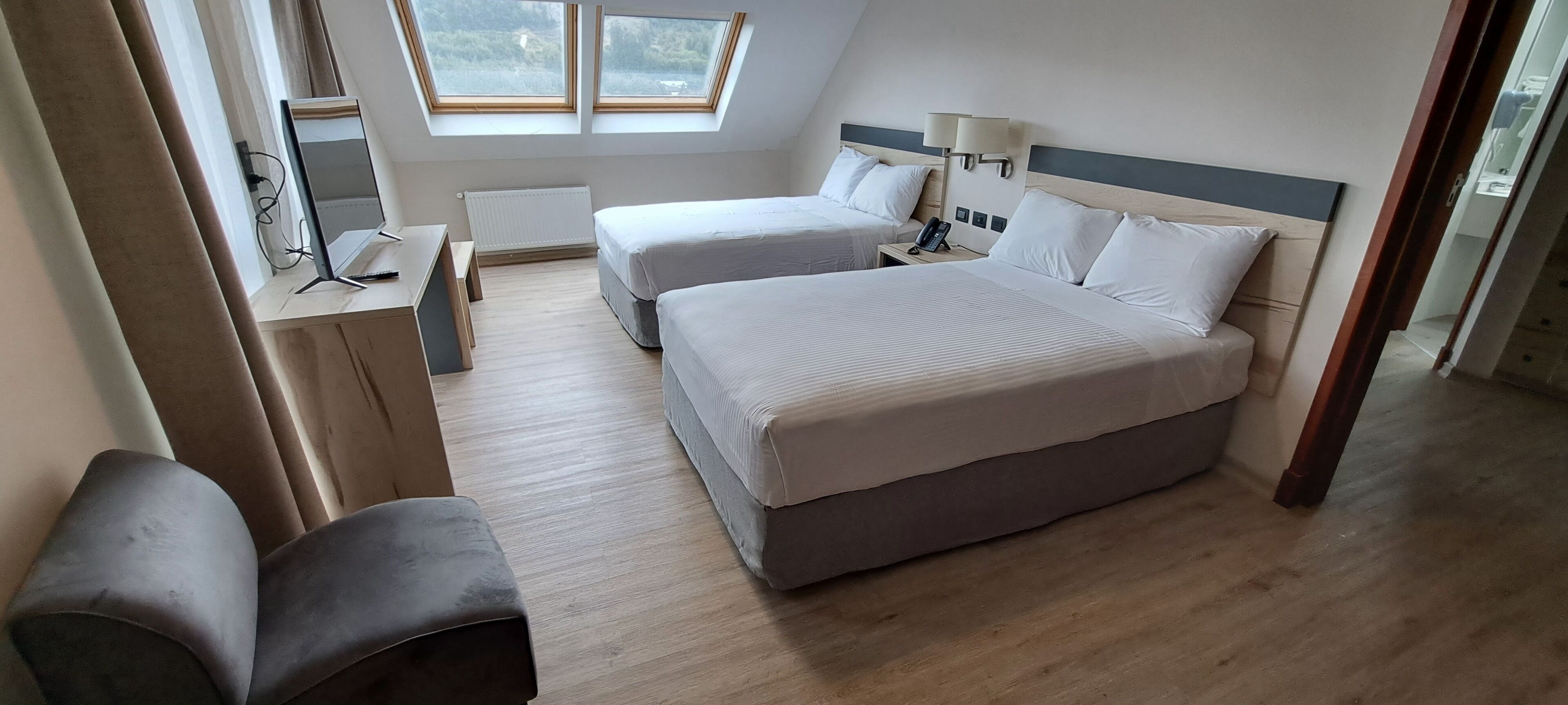 Une chambre d’hôtel avec deux lits, un bureau, une chaise et une fenêtre donnant sur un paysage agréable.