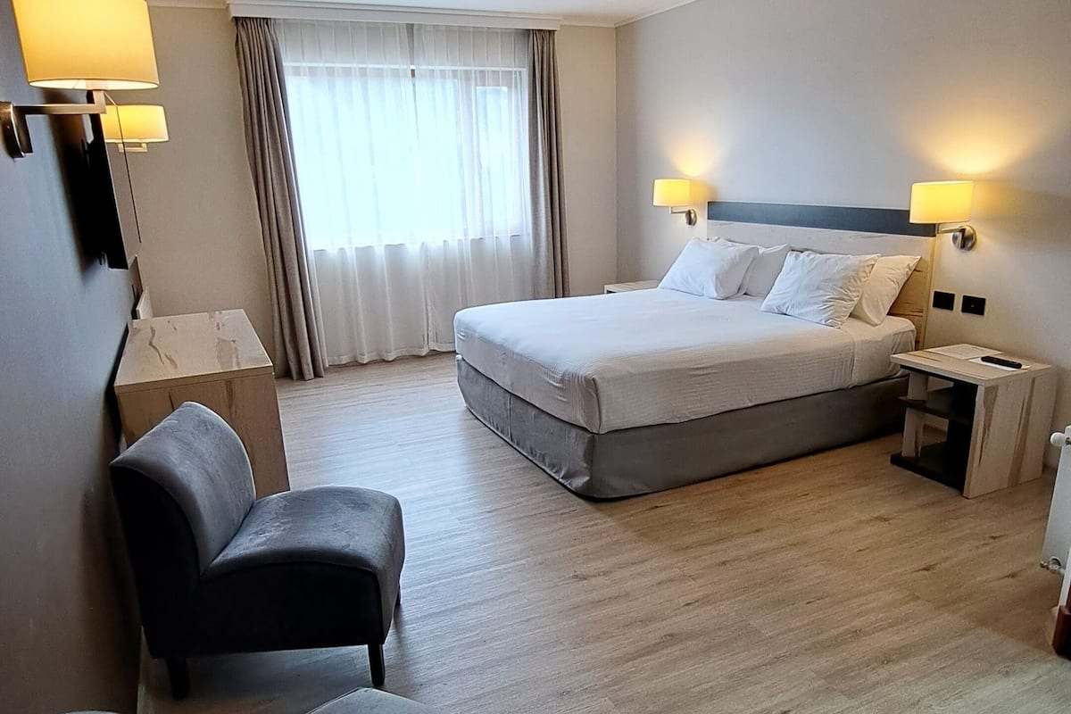 A hotel room with a bed, a sofa, a desk, and a lamp.