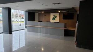 Un área de recepción moderna con un mostrador de madera, una obra de arte abstracta verde y un amplio ventanal con vistas al exterior.
