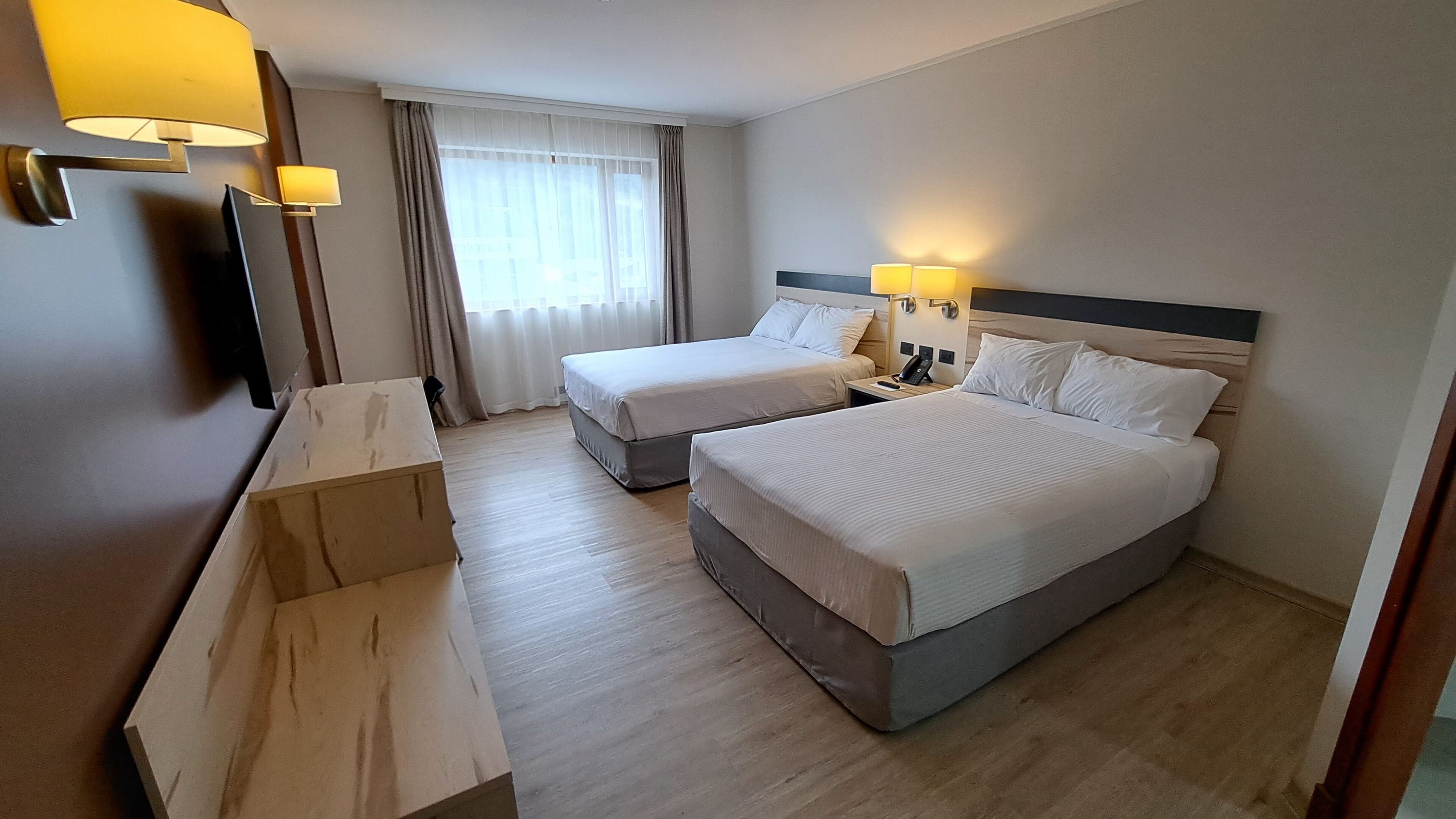 A hotel room with two beds, a desk, a chair, and a large window with curtains.