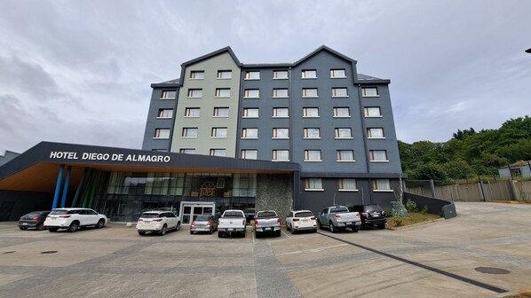 Un immeuble hôtelier à plusieurs étages, doté d’une façade moderne, un parking où sont garées plusieurs voitures, et une enseigne indiquant « HÔTEL DIEGO DE ALMAGRO ».