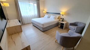 Una habitación de hotel con cama, mesita de noche, lámpara, silla y escritorio.