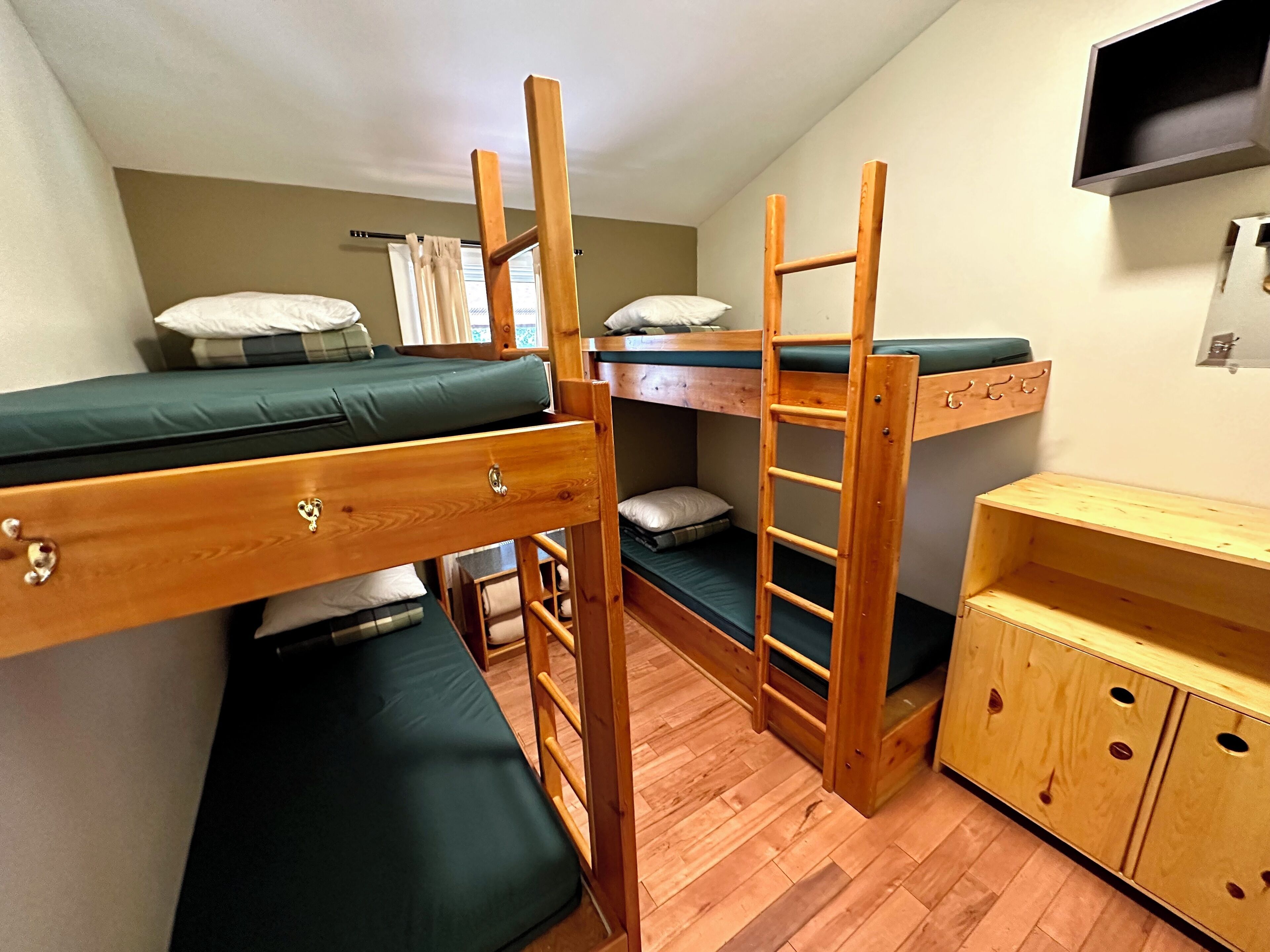 Une chambre de dortoir avec des lits superposés, un bureau en bois et un téléviseur fixé au mur.