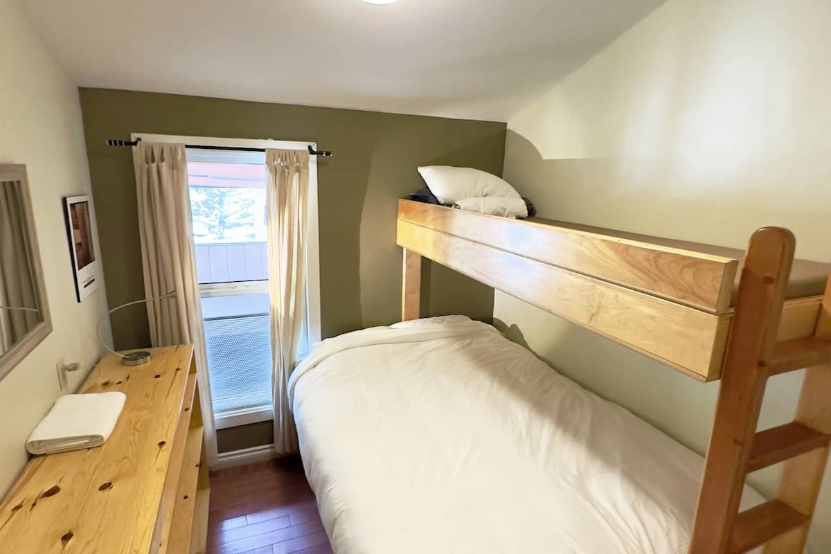 A bunk bed with a wooden ladder, a desk with a white towel, and a window with curtains.