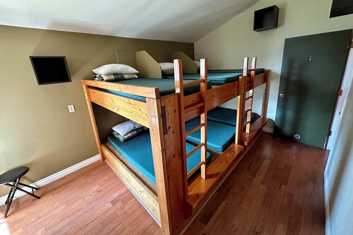 A bunk bed room with a wooden frame, a green mattress, and a white pillow.