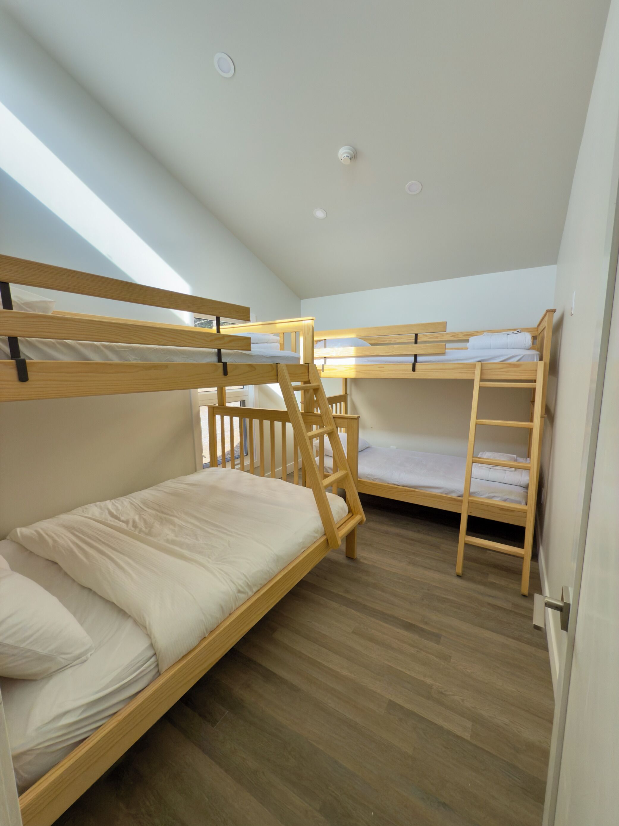 Een studentenkamer met stapelbedden, houten vloeren en een dakraam.