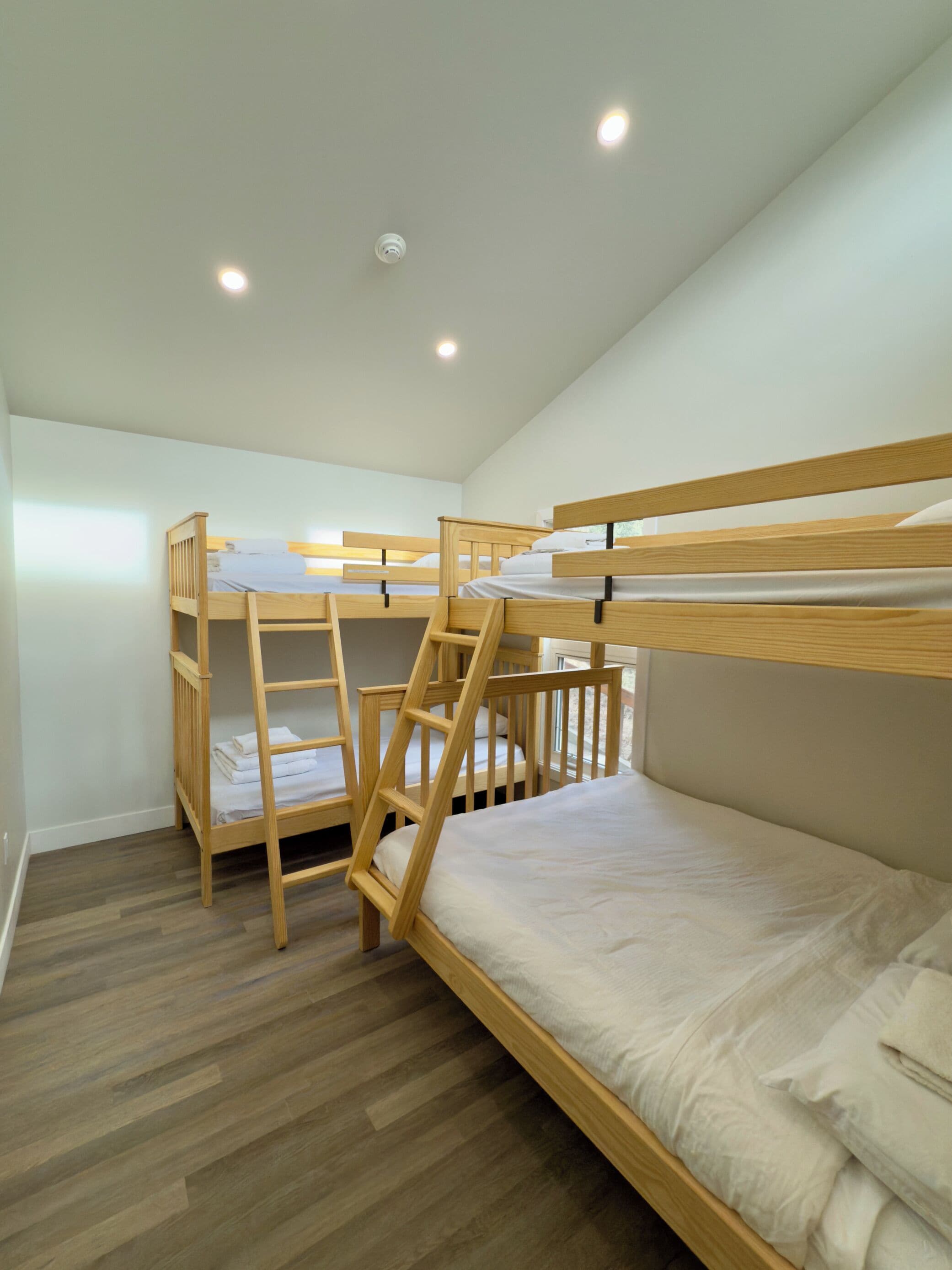 Habitación con literas, una escalera de madera, ropa de cama blanca y suelo de madera.