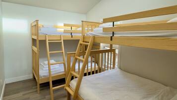 Une chambre avec un lit superposé, une échelle en bois, du linge de lit blanc et un plancher en bois.