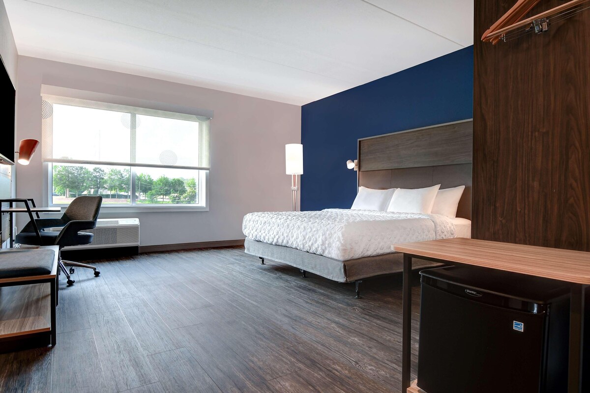 Une chambre d’hôtel moderne équipée d’un lit, d’un bureau, d’une chaise et d’un petit réfrigérateur.