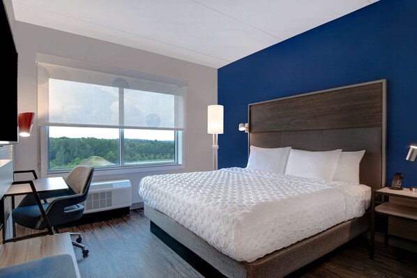 Habitación de hotel con una cama grande, un escritorio, una silla, un ventanal con vistas a árboles y una pared de acento azul.