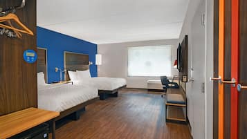Une chambre d’hôtel avec deux lits, un bureau, une chaise, une télévision et une fenêtre avec des stores.