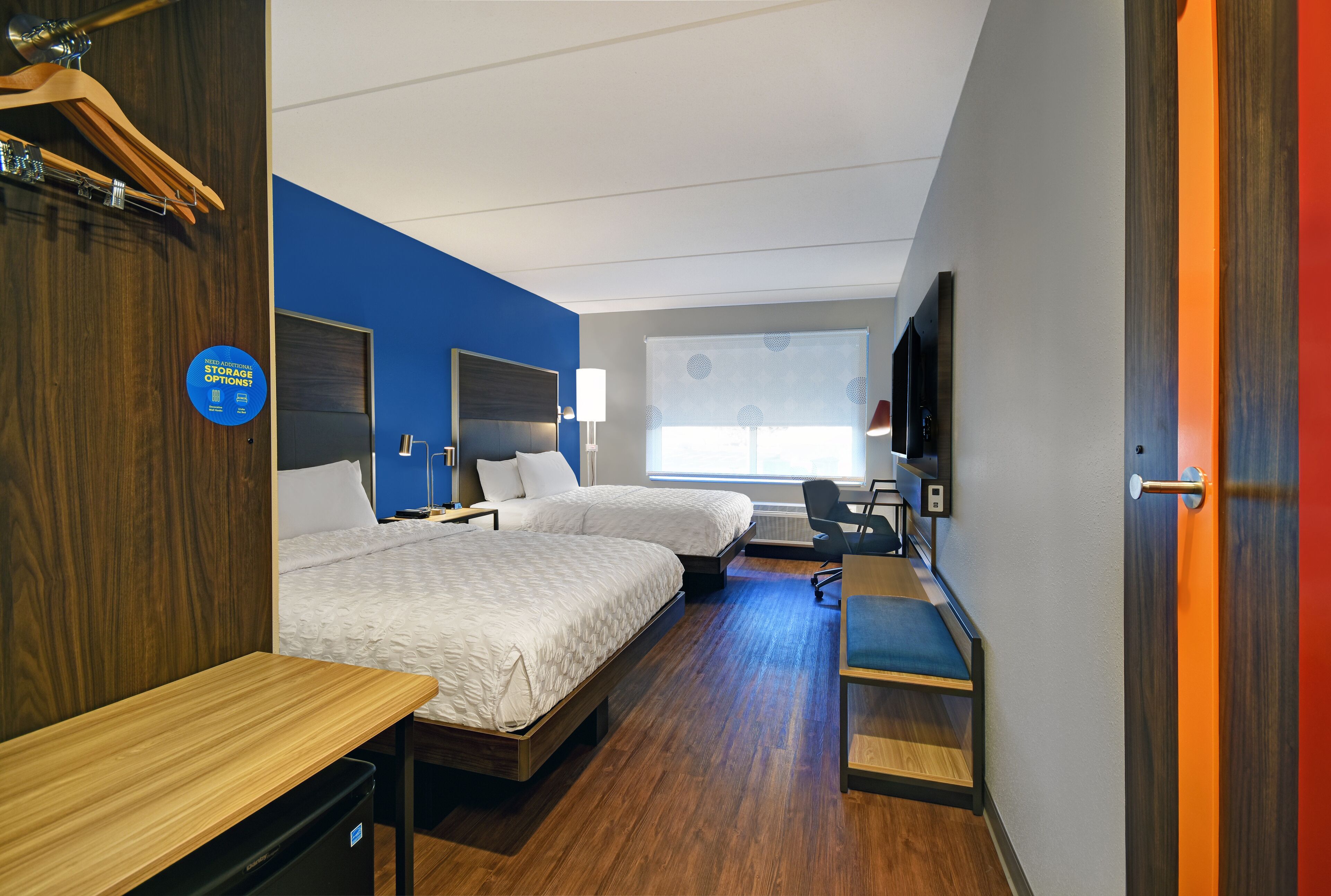 A hotel room with two beds, a desk, a chair, a TV, and a wardrobe.