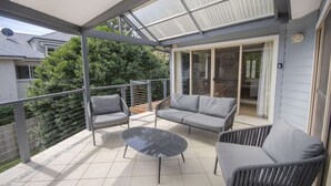 A covered balcony with grey outdoor furniture, including a sofa and chairs, and a glass table. - "Happy Ours" - Walking Distance to Shops & Beach (AVOCA BEACH)