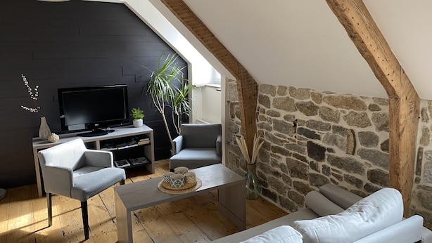 Un salon moderne de style industriel, avec un mur en pierre, des poutres en bois, un téléviseur à écran plat et différents types de sièges.