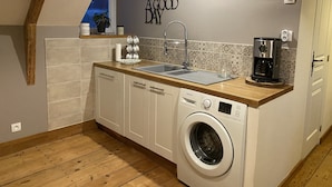 Une cuisine compacte équipée d’un lave-linge, d’un évier et d’une machine à café.
