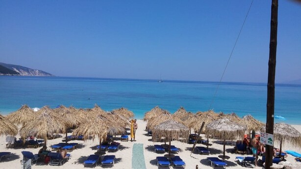 A beach with thatched umbrellas and sun loungers, a clear blue sea, and a distant sailboat. - Villa "Sofia" with an amazing view at Angonas. (Agκona)
