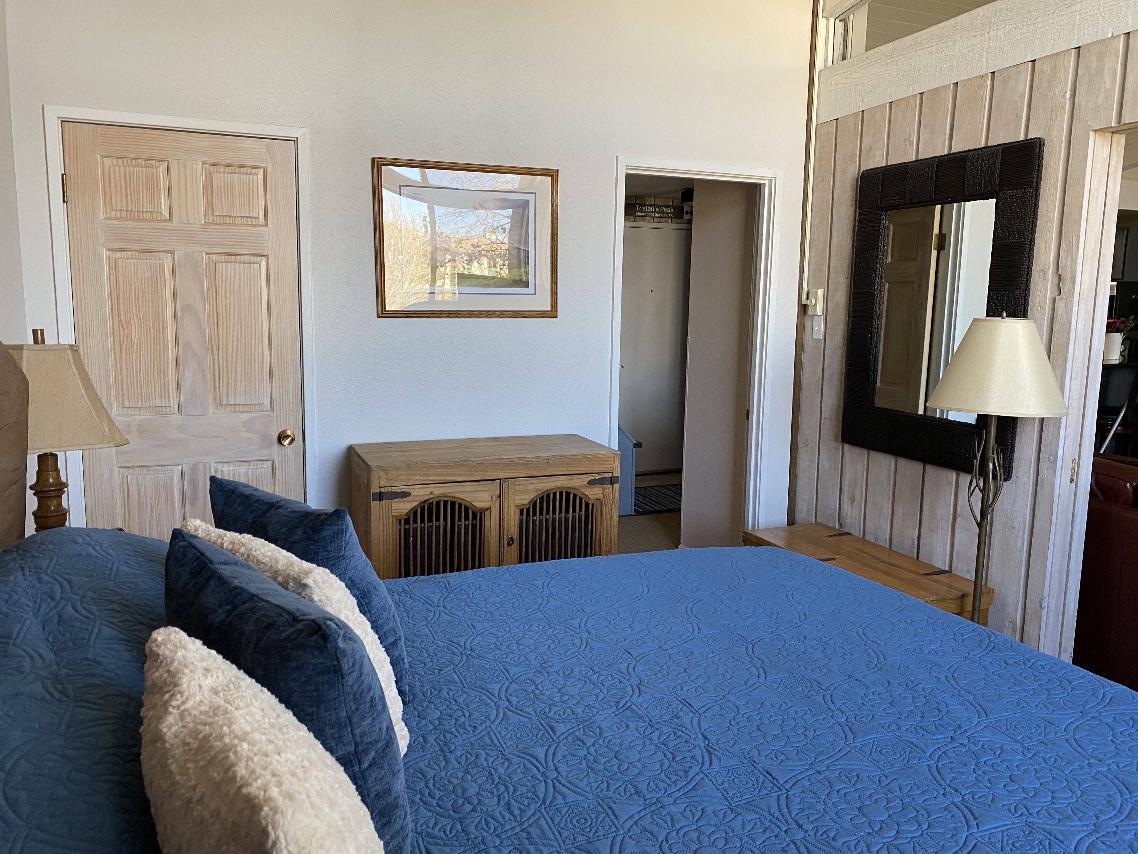A bedroom with a large bed, a wooden cabinet, a mirror, and a door leading to a closet.