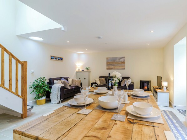 A dining area with a wooden table set for a meal, a sofa, a fireplace, and a staircase.