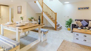 Een moderne woonkamer met een houten trap, een eethoek met een tafel gedekt voor twee personen, en een bank met kussens.